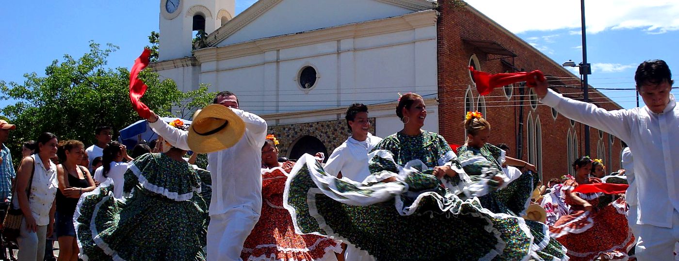 Parejas bailando danza folclórica con trajes típicos frente a la iglesia de Melgar
